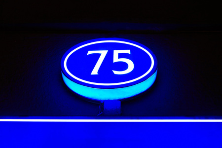 The glowing blue light of the number 75 indicates the number of the house in the darkの写真素材