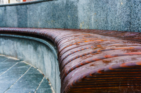 Wooden bench wavy form with puddles after the rain on the street close up