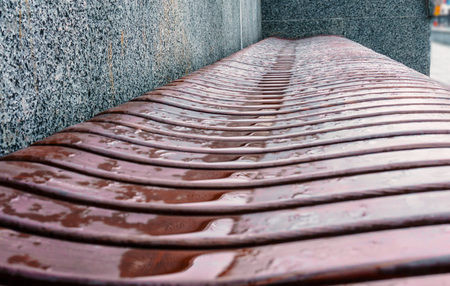 Wooden bench wavy form with puddles after the rain on the street close upの写真素材