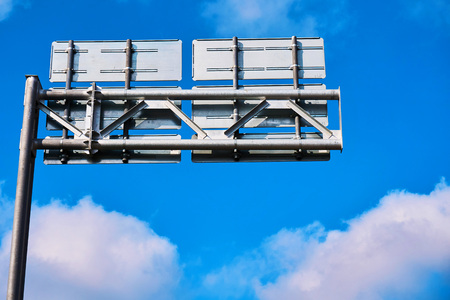 A high road sign from thick metal and a complex construction against the backdrop of the blue sky and cloudsの写真素材