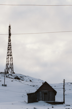 High radio tower in winter near an old wooden house on a high hillの写真素材