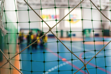 Young football players in bright uniforms play football in a closed sports complex behind a football gate with a close-up gridの写真素材