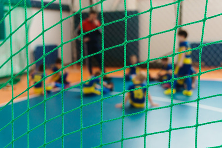 Young football players in bright uniforms play football in a closed sports complex behind a football gate with a close-up gridの写真素材