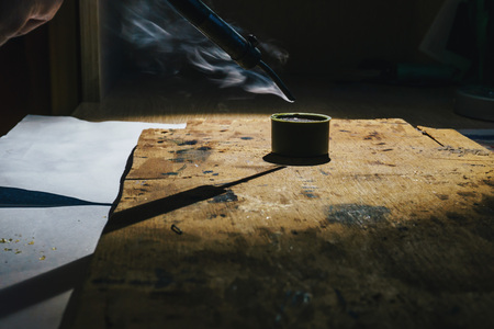 Working with a hot metal soldering iron at home under the spotlight and smoke that comes from liquid rosinの写真素材