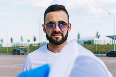 A young guy with a beard in his white T-shirt and shorts is holding a flag of Russia that is developing in the windの写真素材