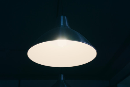 The black chandelier under the ceiling shines in a dark room with white lightの写真素材