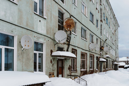 Old dilapidated and partially destroyed houses in which people still live in the village in the far north in winter under the thick slime of white snowの写真素材