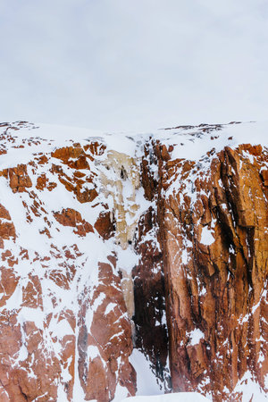 High red rocks rise above the snow-covered coast of the sea in winter in spooky cold and strong wind during an expedition to the Arcticの写真素材