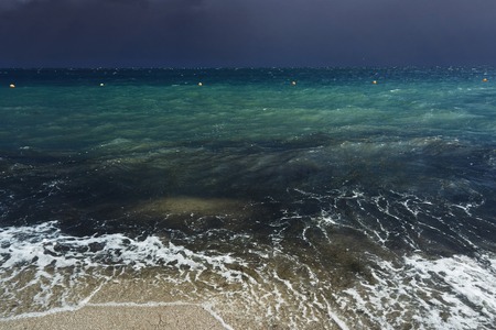 Small waves with foam at the time of storm beginning in the evening on the shore of the dark sea on the beach of the sea resortの写真素材
