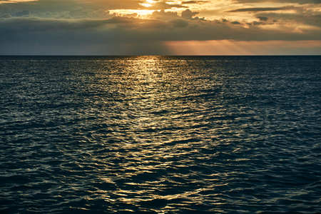 Beautiful bright orange sunset beyond the horizon line of the sea and reflection of the last rays on the surface of the waterの写真素材