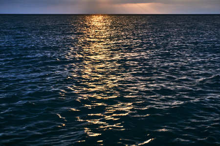 Beautiful bright orange sunset beyond the horizon line of the sea and reflection of the last rays on...