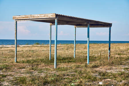 Sunshade and the remains of children's playgrounds on an abandoned beach on the shores of a warm sea that is already overgrown with grass and untidyの写真素材