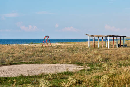 Sunshade and the remains of children's playgrounds on an abandoned beach on the shores of a warm sea that is already overgrown with grass and untidyの写真素材