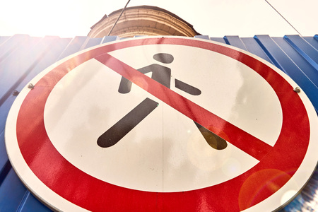 white with red lines and a man sign prohibiting the movement of people in a danger zone on a metal fence of blue colorの写真素材