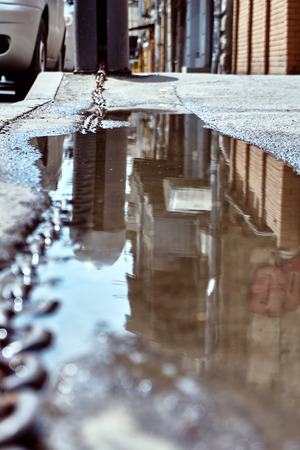 ripage of city streets and buildings in a puddle in uneven asphalt on the road after rain on a summer dayの写真素材