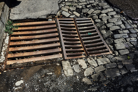 drainage sewer grate on the old road from the broken asphalt and paving blocks wet after the rain in...