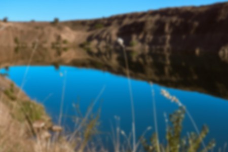 Blurred photo for background. An amazing wild lake without people in a gorge of sand color among the stones and trees with crystal clear blue water on a nice warm summer day in the bright sunの写真素材