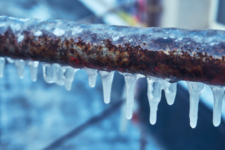 Many small icicles have frozen on a rusty pipe in the street in the winter