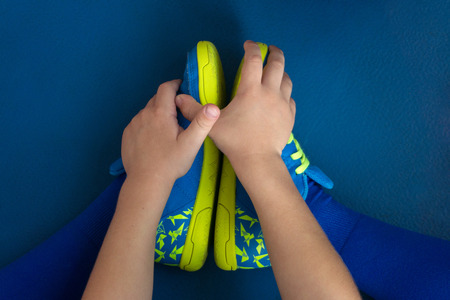 little baby football player in bright sneakers resting on the blue floor in the gym while playing