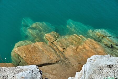 crystal clear blue cool water at the shore of a wild lake in a quarry without people with steep rocky beaches and large boulders on a summer warm dayの写真素材