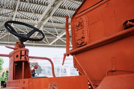 tractor operator's workplace with steering wheel and levers on an old orange tractor without glazing under the open skyの写真素材