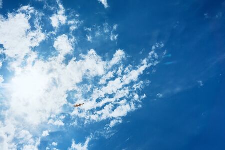 A large kite floats high in the sky among the clouds against the blue sky and the bright summer sun and it is controlled by two white ropes going to the groundの写真素材