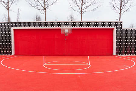 a basketball hoop with a net against a bright red wall and floor on a modern sports ground with...