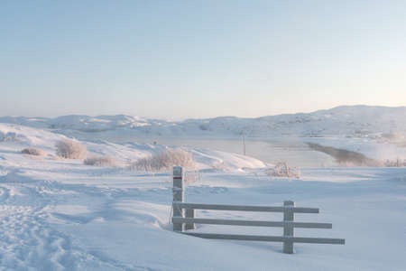 broken wooden fence in deep white snow on the outskirts of the village beyond the Arctic Circle on a frosty sunny dayの写真素材