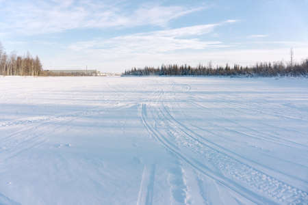 a large empty area covered with snow and snowmobile tracks. A guy in a yellow jacket rides a snowmobileの写真素材