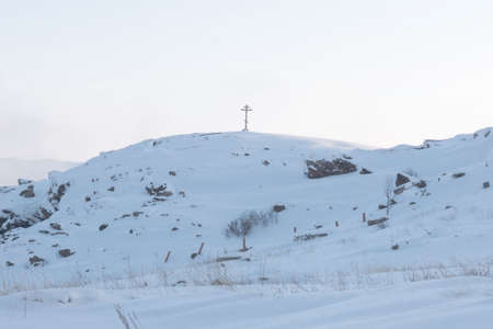 a valley covered with deep white snow and hills in dense fog with an Orthodox cross upstairs on a frosty winter day in the far northの写真素材