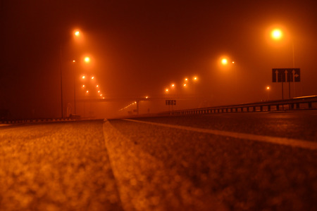Foggy night in the big city, the empty street lighting lanterns. Close up view from the level of the dividing lineの写真素材