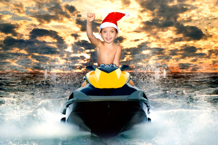 Little boy in Santa hat riding a water scooter on the waves.の写真素材