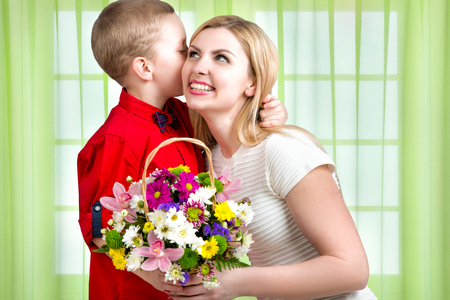 Young beautiful mother with her son.To whisper a secret in your ear. Woman and child with bouquet of flowers. Spring family holiday concept. Women's day.の写真素材