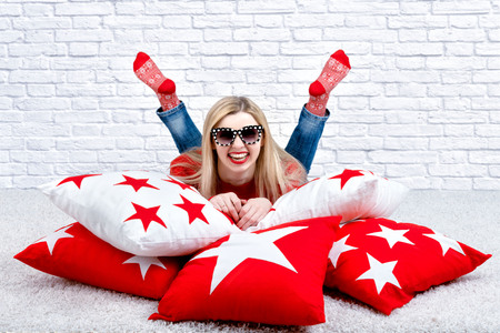 Beautiful young blonde woman in glasses lying on the pillow. Beautiful pillows to decorate the interior of the house. Pillow with star ornament.の写真素材
