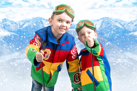 Two brothers of the boy snowboarder in bright ski jackets and goggles is skiing in the mountains.の写真素材