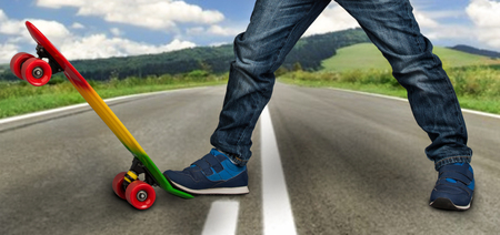 A young skateboarder in sneakers and jeans, standing on his skate. Closeup of the skateboard and feet.の写真素材