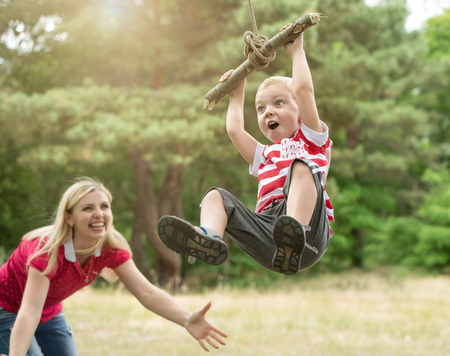 Little boy riding on a makeshift swing in the woods.Mom looks at the flight of a little son. ?の写真素材