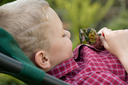 The boy looks at his reflection in sunglasses.の写真素材