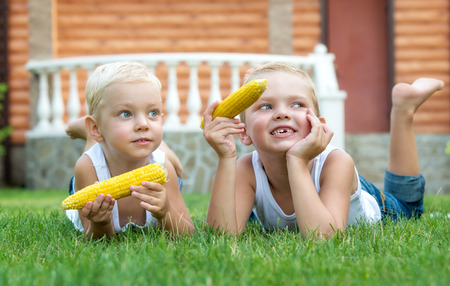 Two brothers lying on the grass and eat corn on the cob in the gardenの写真素材