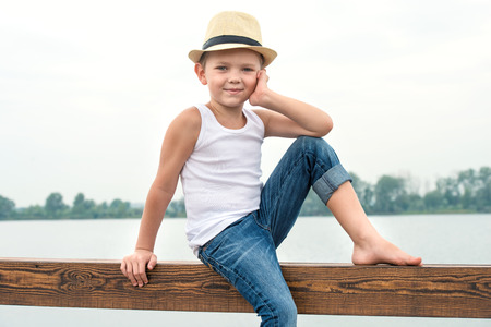 A boy in a straw hat sitting on the pier .Summer vacation on the lakeの写真素材