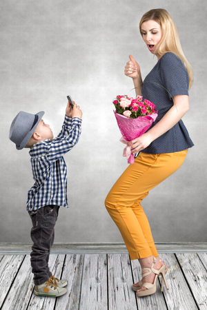 Little boy taking pictures on a mobile phone your mom with a bouquet of roses.Spring, concept of family vacation. Women's day, mother's day.の写真素材