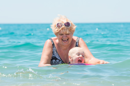 Grandmother and little grandson swim in the sea.The baby in the bouncy multicolored circle.Summer vacation.の写真素材