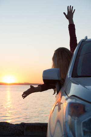 A young woman looks out the car window at the sunset on the sea.の写真素材