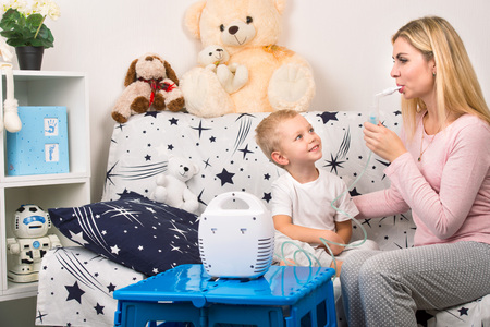 Young woman with son doing inhalation with a nebulizer at home. Mother of a young child making inhalationの写真素材