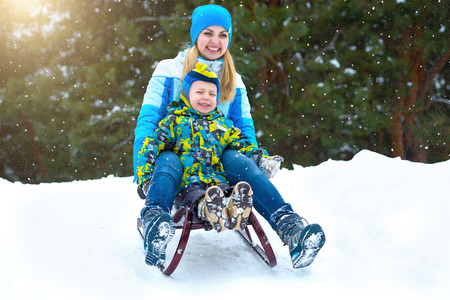 Mother and son ride on sleigh .Child play in snowy forest. Outdoor winter fun.の写真素材