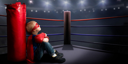 A child in a superhero costume sits in the ring and dreams of boxing victories.の写真素材