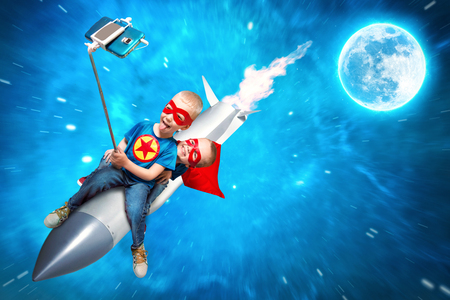 Children in superhero costumes fly in space on a rocket and shoot a selfie on a mobile phone.の写真素材