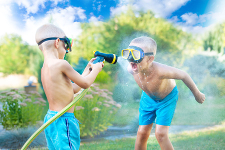 Two brothers play on a summer day in the garden. Children are splashing with a garden hose.の写真素材
