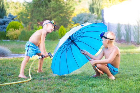 Two brothers play on a summer day in the garden. Children are splashing with a garden hose.の写真素材