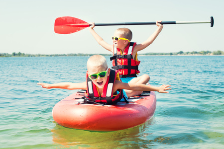 Two brothers swimming on stand up paddle board.Water sports, active lifestyle.の写真素材